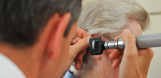 Close-up view of audiologist examining male patient's ear with otoscope. 
