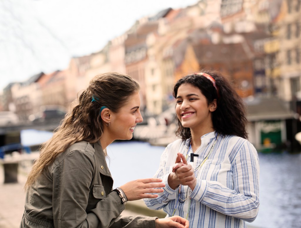 Two woman by a canal. One of the women has a cochlear implant. The women are talking and smiling.