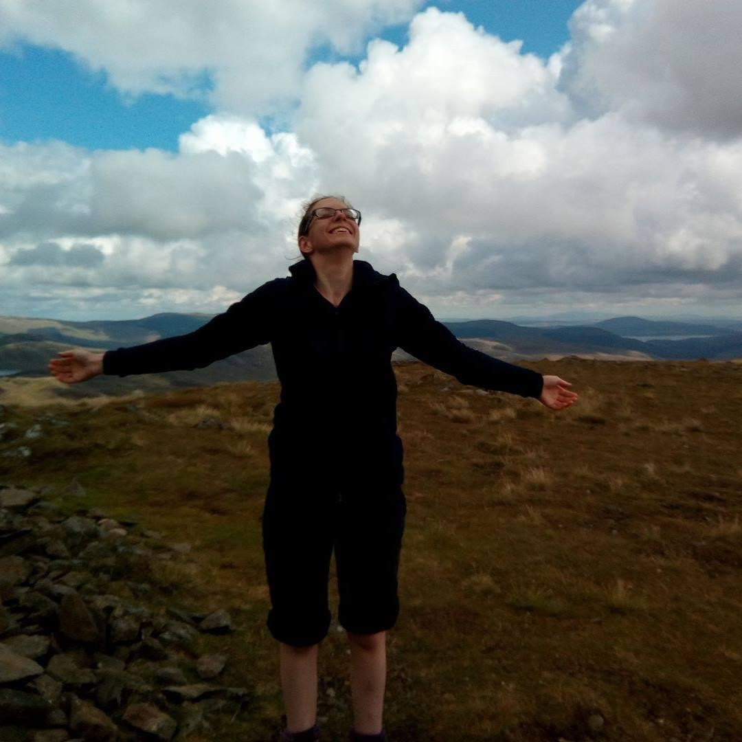Rachel in walking clothes, smiling with her arms outstretched, her head tilted backwards