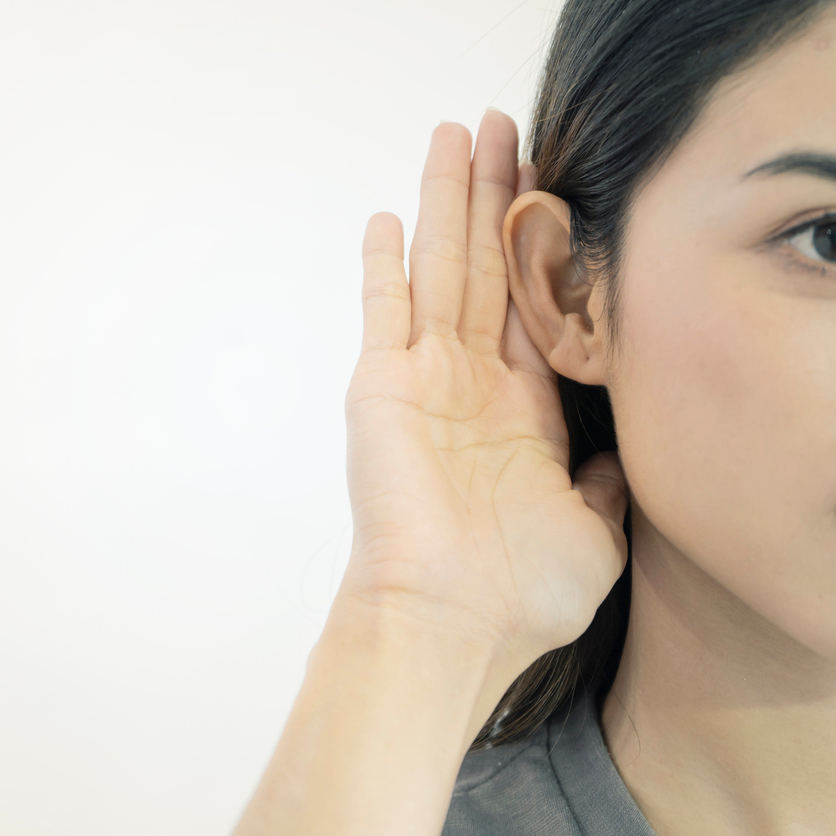 Half of a woman's face with cupped hand behind her ear, on white background.