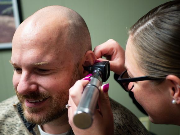 Man having his ear checked by a hearing healthcare professional using an otoscope. Photo by Anthony Camerlo on Unsplash.