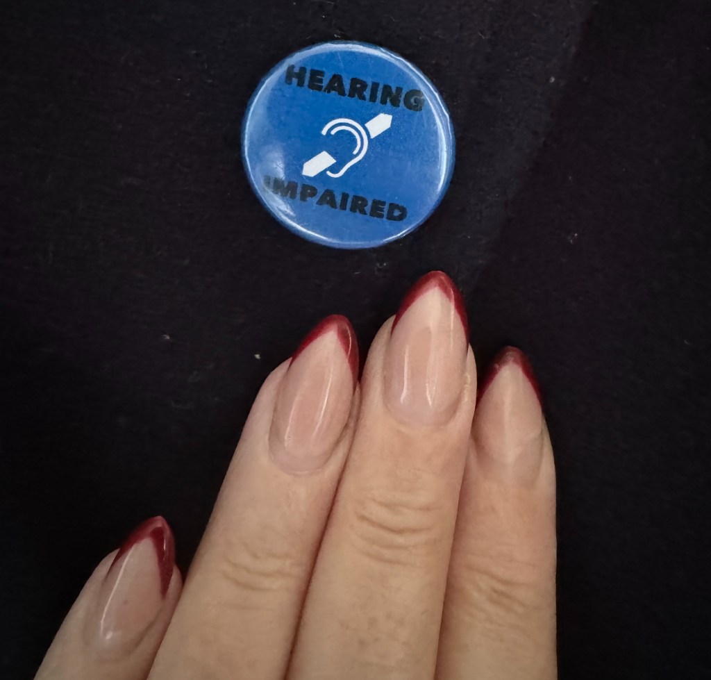 A hand with long nails and a blue badge which read "Hearing Impaired."